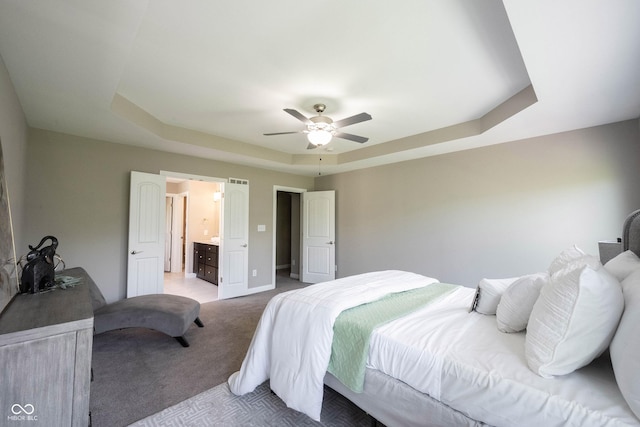bedroom featuring light colored carpet, a raised ceiling, a ceiling fan, and ensuite bathroom