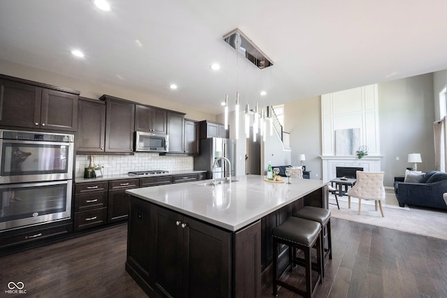 kitchen with stainless steel appliances, a center island with sink, open floor plan, a kitchen breakfast bar, and a sink