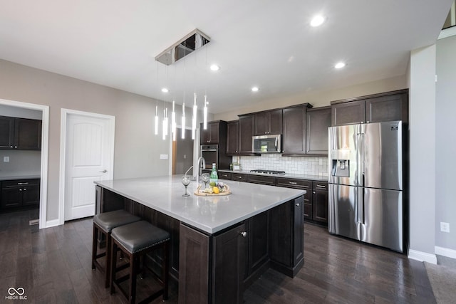 kitchen featuring appliances with stainless steel finishes, a center island with sink, backsplash, dark wood-style flooring, and recessed lighting