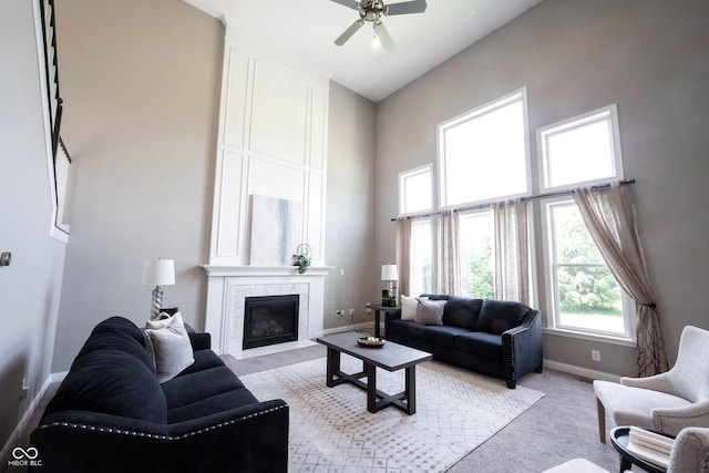 living area with light colored carpet, baseboards, a high end fireplace, a high ceiling, and ceiling fan