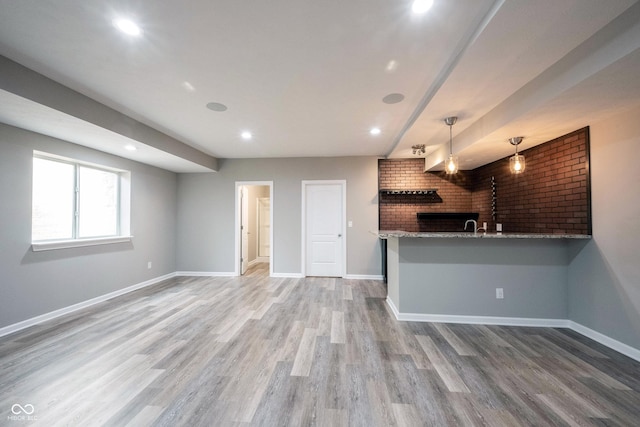 kitchen with baseboards, light wood-style floors, light stone countertops, a peninsula, and hanging light fixtures