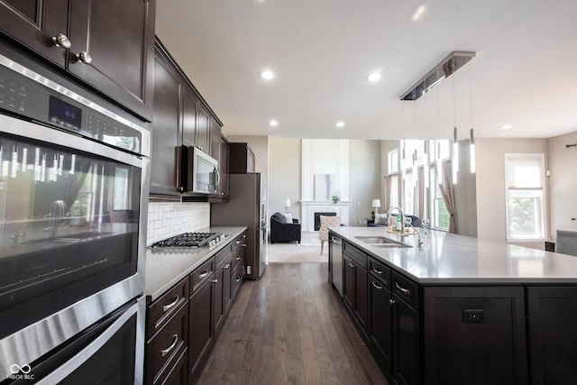 kitchen with a sink, stainless steel appliances, open floor plan, dark wood finished floors, and light countertops