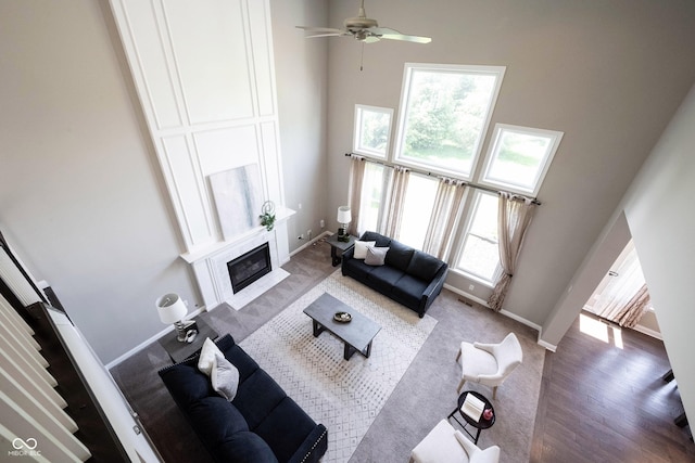carpeted living room featuring a towering ceiling, a premium fireplace, a ceiling fan, and baseboards