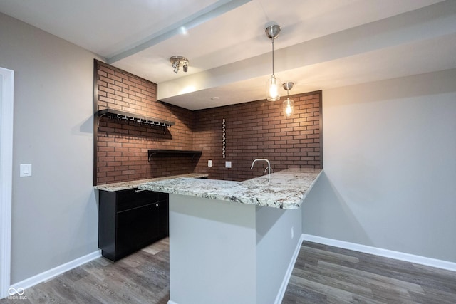 kitchen with light wood-type flooring, a peninsula, baseboards, and brick wall