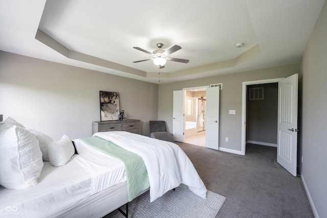 carpeted bedroom featuring baseboards, a tray ceiling, ensuite bathroom, and a ceiling fan