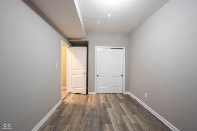 unfurnished bedroom featuring wood finished floors, baseboards, and a closet