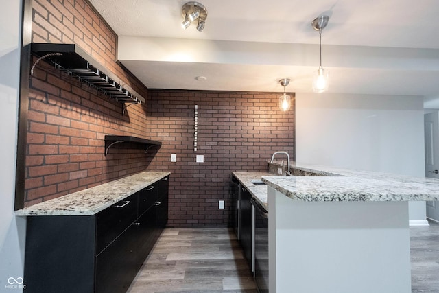 kitchen featuring brick wall, light wood-type flooring, dark cabinetry, a sink, and decorative light fixtures