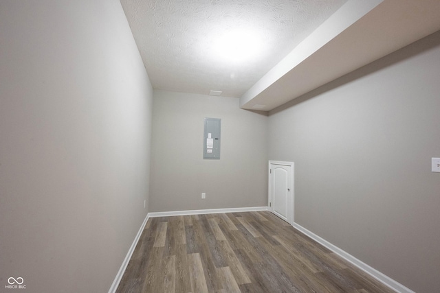 additional living space featuring wood finished floors, a textured ceiling, baseboards, and electric panel