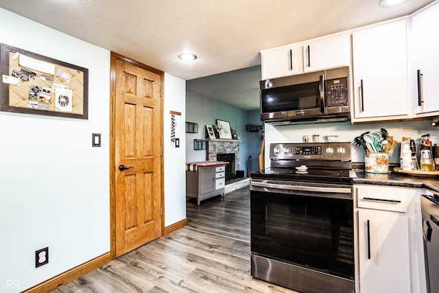 2965 E 1100 N, Pendleton, IN 46064 - kitchen featuring stainless steel appliances, light wood-style floors, white cabinetry, a stone fireplace, and dark countertops