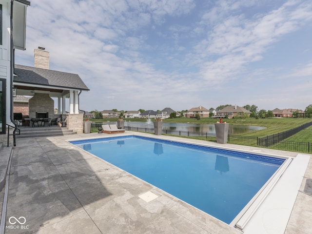 view of swimming pool with an outdoor stone fireplace, a patio area, a water view, and a residential view