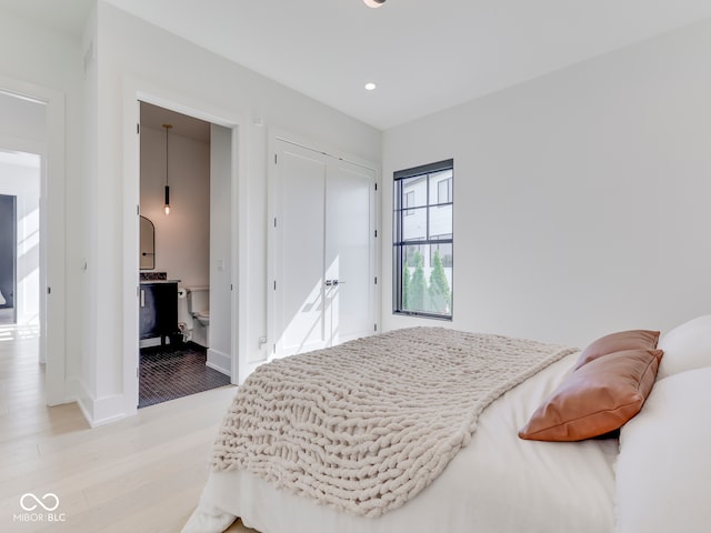 bedroom with light wood-type flooring, recessed lighting, a closet, baseboards, and ensuite bath