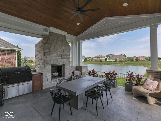 view of patio / terrace with an outdoor stone fireplace, a ceiling fan, a water view, and fence