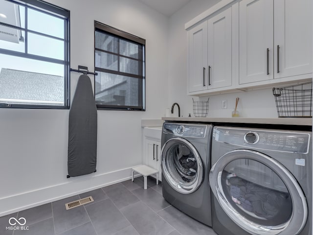 clothes washing area with washing machine and dryer, cabinet space, baseboards, and dark tile patterned flooring