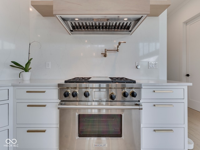 kitchen featuring high end stove, wall chimney range hood, white cabinetry, and light countertops