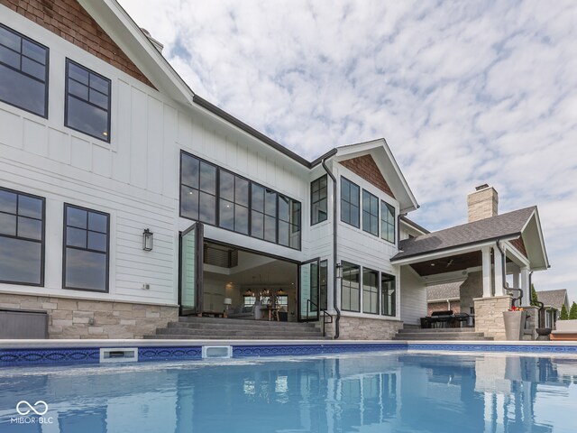 back of house with an outdoor pool, stone siding, and a patio