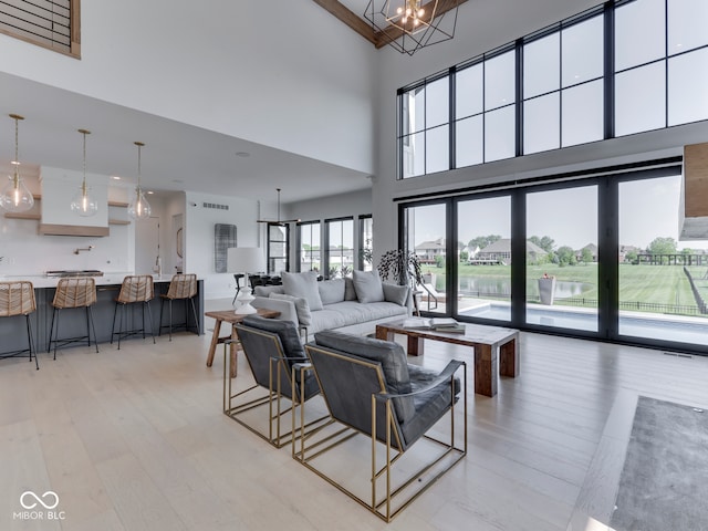 living area with a towering ceiling, light wood finished floors, a chandelier, and a water view