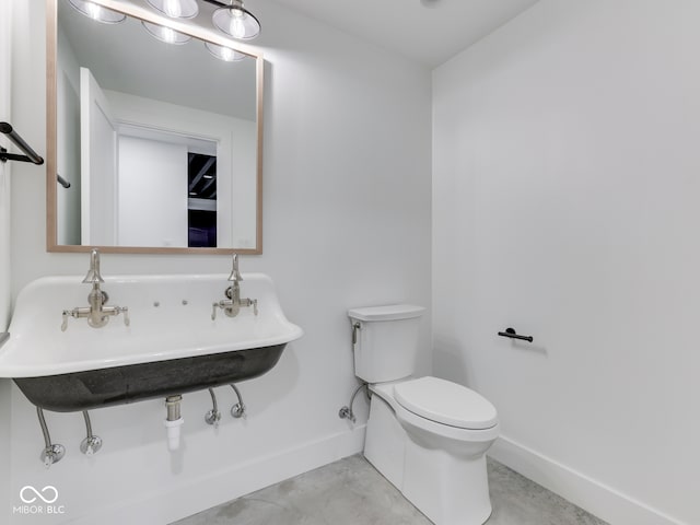 bathroom with baseboards, toilet, concrete flooring, and a sink