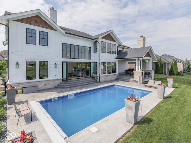 back of property with a patio, board and batten siding, a chimney, stone siding, and exterior kitchen