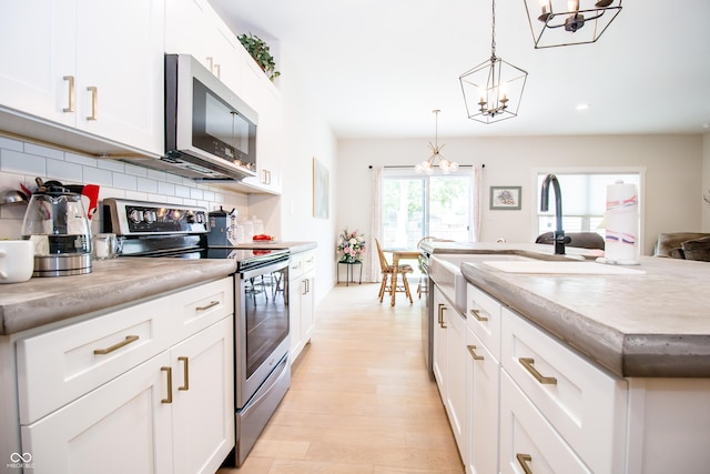 2686 Lafayette Ave, Columbus, IN 47201 - kitchen featuring stainless steel appliances, a chandelier, decorative backsplash, white cabinetry, and light wood-style flooring