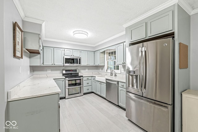 12388 Camberley Ln, Carmel, IN 46033 - kitchen featuring stainless steel appliances, a sink, a textured ceiling, ornamental molding, and light wood-type flooring