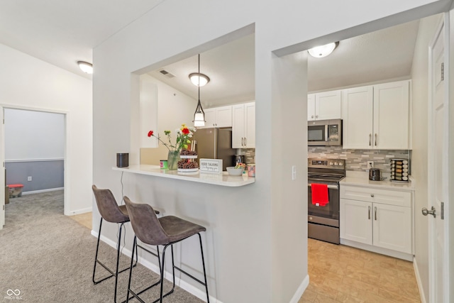 8910 Hunters Creek Dr Unit 207, Indianapolis, IN 46227 - kitchen featuring appliances with stainless steel finishes, a breakfast bar, backsplash, white cabinets, and light countertops