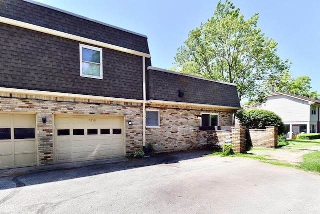 1310 Kings Cove Ct, Indianapolis, IN 46260 - view of property exterior with mansard roof, a shingled roof, brick siding, asphalt driveway, and a garage