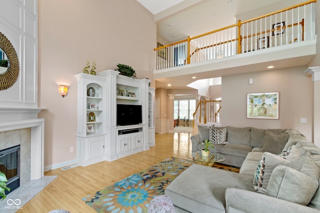 14094 Pecos Ct, Carmel, IN 46033 - living area with light wood-style floors, a fireplace, a towering ceiling, baseboards, and decorative columns