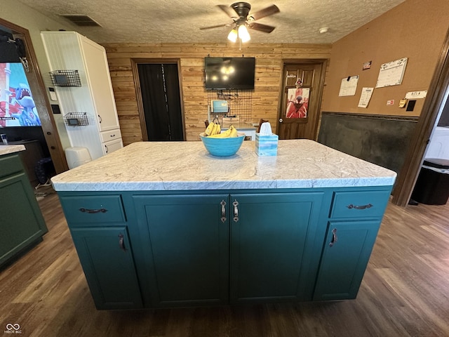 kitchen with wooden walls, a textured ceiling, blue cabinetry, a ceiling fan, and dark wood-type flooring