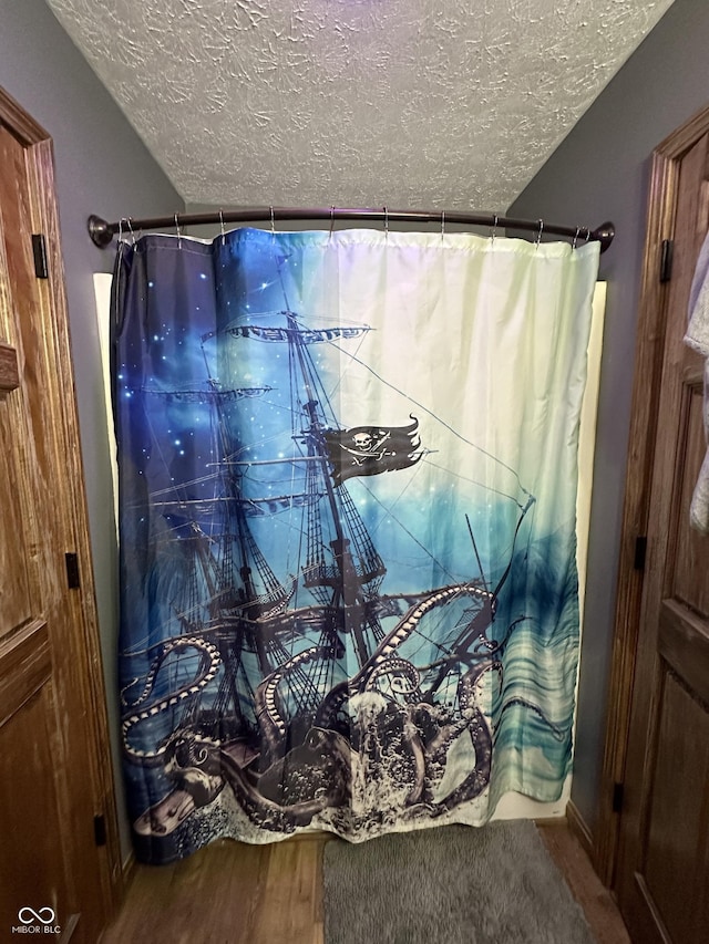 bathroom with a textured ceiling, wood finished floors, and curtained shower