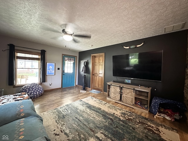living area featuring a textured ceiling, wood finished floors, ceiling fan, and baseboards