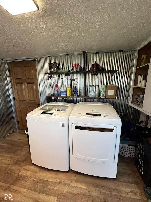 laundry area with washing machine and clothes dryer, a textured ceiling, and wood finished floors