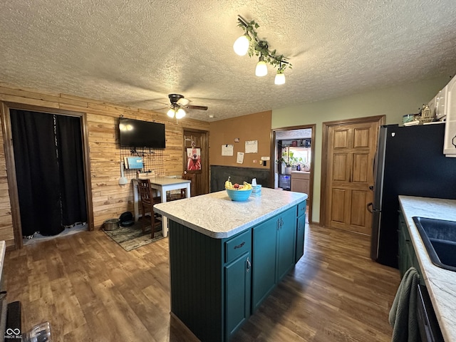 kitchen featuring ceiling fan, a textured ceiling, wood finished floors, wooden walls, and a center island