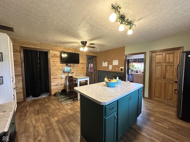 kitchen with freestanding refrigerator, blue cabinetry, dark wood-style flooring, wooden walls, and a ceiling fan