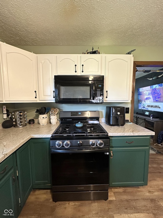 kitchen with black microwave, stainless steel gas range oven, green cabinets, wood finished floors, and a textured ceiling