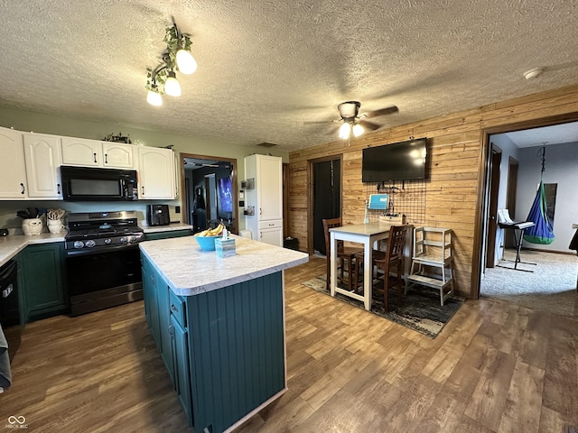 kitchen featuring stainless steel gas stove, black microwave, white cabinetry, ceiling fan, and wooden walls