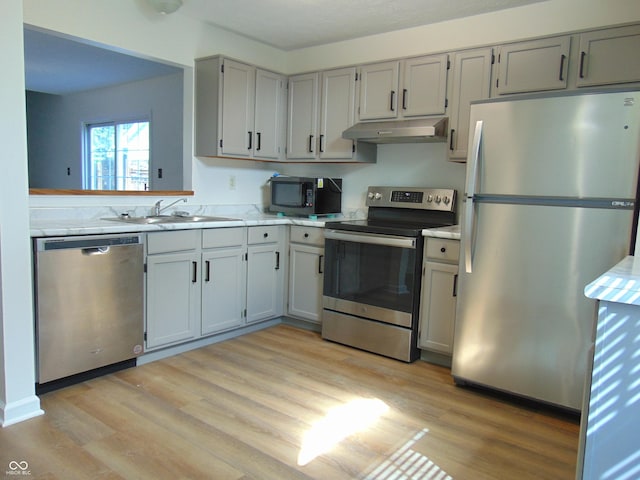 kitchen with stainless steel appliances, under cabinet range hood, a sink, light countertops, and light wood-style floors