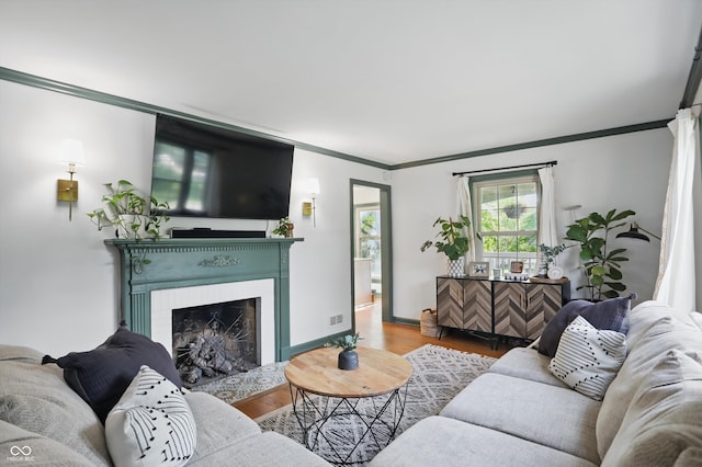 living room featuring crown molding, wood finished floors, a fireplace with flush hearth, and baseboards