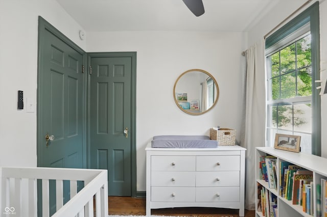 bedroom with wood finished floors, a crib, and a ceiling fan