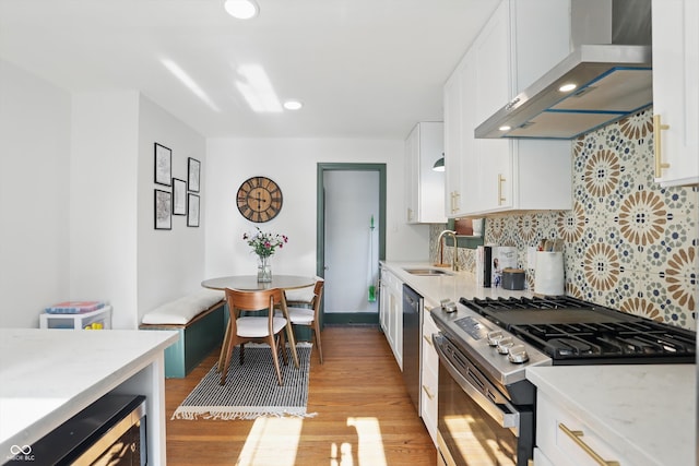 kitchen with appliances with stainless steel finishes, wall chimney range hood, a sink, decorative backsplash, and white cabinetry