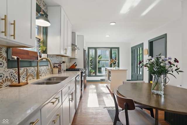 kitchen with a sink, light wood-style floors, backsplash, light stone countertops, and white cabinets