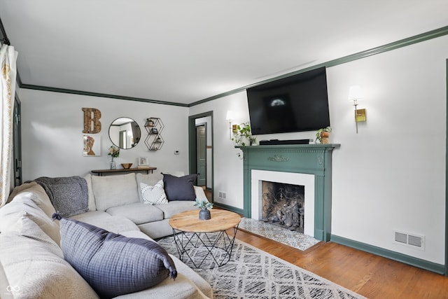 living area featuring a fireplace with raised hearth, crown molding, wood finished floors, and baseboards
