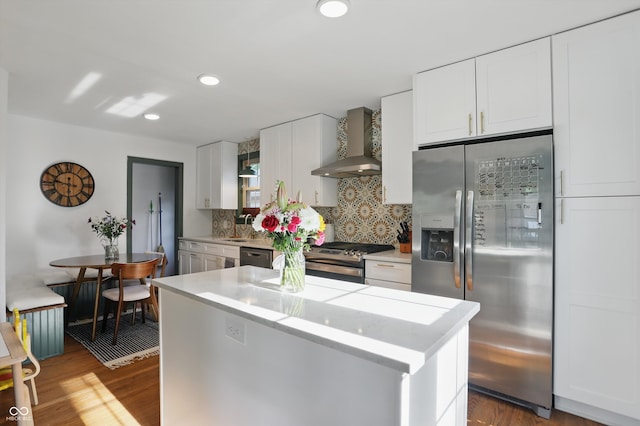 kitchen with appliances with stainless steel finishes, wall chimney exhaust hood, light countertops, backsplash, and wood finished floors