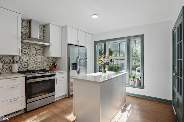 kitchen with stainless steel appliances, wall chimney exhaust hood, light countertops, backsplash, and white cabinetry