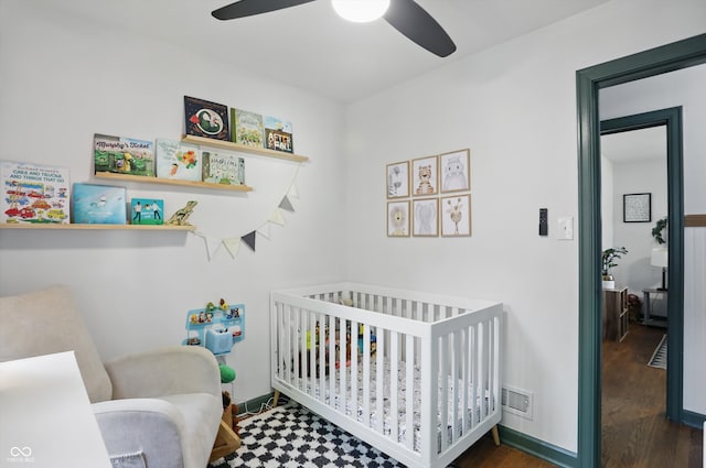 bedroom featuring a crib, wood finished floors, ceiling fan, and baseboards