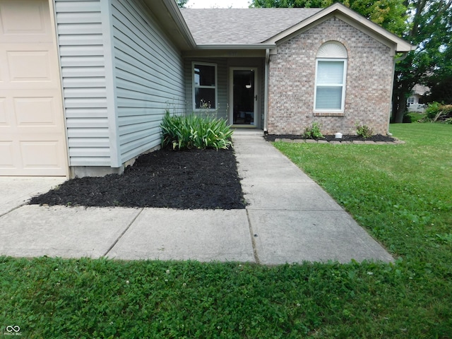 1612 Prairieview Ln, Greenfield, IN 46140 - view of exterior entry featuring a garage, a lawn, brick siding, and a shingled roof