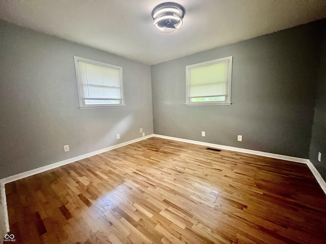 unfurnished room featuring healthy amount of natural light, wood finished floors, and baseboards