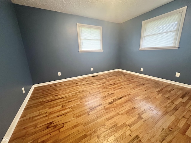 spare room with wood finished floors, a textured ceiling, and baseboards