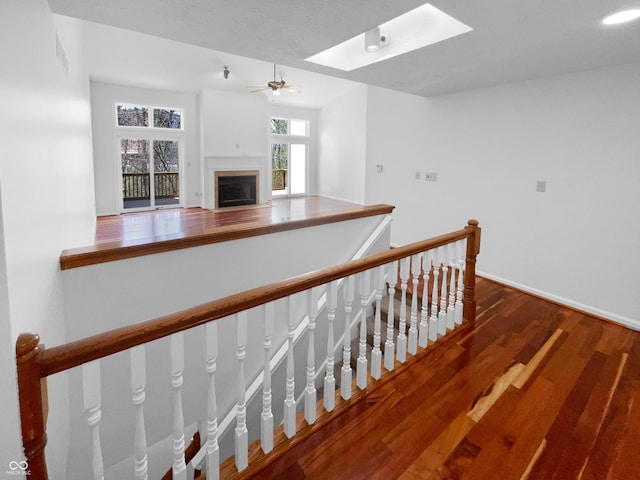 staircase with wood finished floors, a skylight, a fireplace, baseboards, and ceiling fan