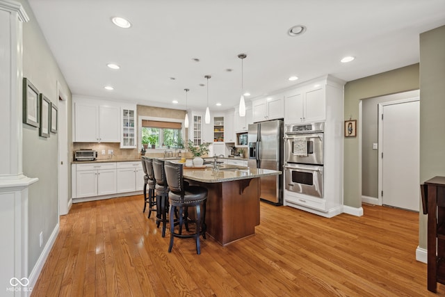 8330 Claridge Rd, Indianapolis, IN 46260 - kitchen with appliances with stainless steel finishes, light wood finished floors, a sink, light stone counters, and glass insert cabinets