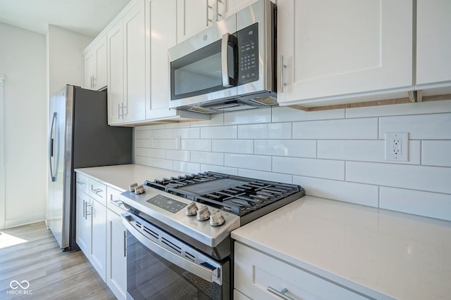 kitchen with stainless steel appliances, white cabinetry, light countertops, light wood-style floors, and decorative backsplash